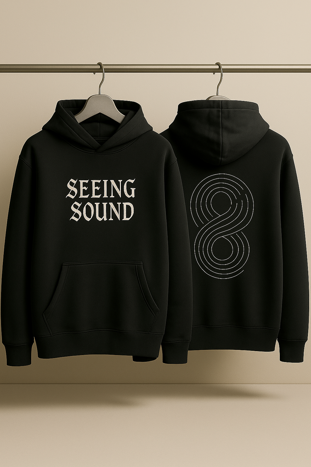 Black hoodie with 'SEEING SOUND' text on front and circular design on back, hanging against a beige background.